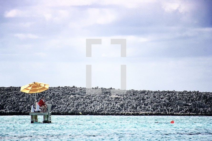 lifeguard sitting on chair stand with umbrella in the ocean.