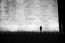 Silhouette of a man standing in front of a stone wall.