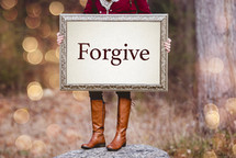woman holding a frame with the word forgive 