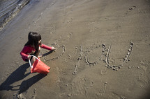 Little girl writing "heart you" in the sand on the beach