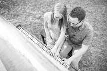 a couple sitting at a piano outdoors 