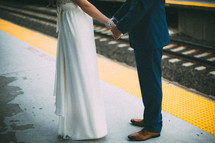 legs and torso of a bride and grooms holding hands 
