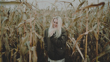 a woman in a coat standing in a corn field 