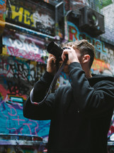 man taking a picture in a graffiti filled alley 