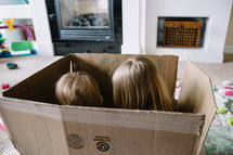 Two children playing in an empty box.