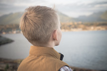 A young boy child taking in the view standing on a lake shore in fall. 