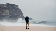 a man standing on a shore watching waves crash into rocks 