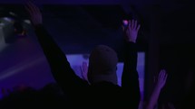 raised hands in an audience and purple stage lights 