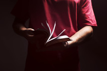 man flipping through the pages of a Bible in a dark room.