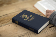 A person studying the Bible next to The Book of Mormon.