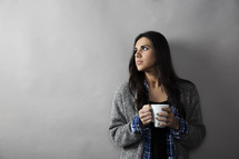 woman holding a coffee mug and looking away in thought. 