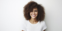 Confident young woman with curly hair and glasses smiling on a white background.