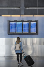 a woman looking at the departure list at an airport 