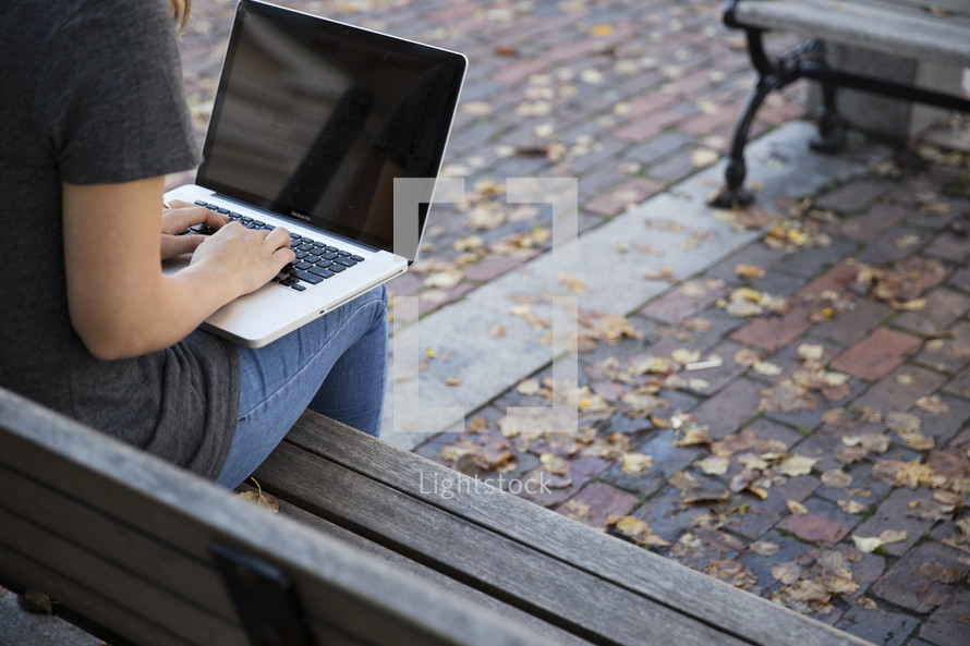 young woman sitting on a bench with a laptop on her lap 
