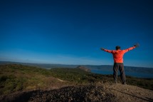 man with outstretched arms standing on a mountaintop 