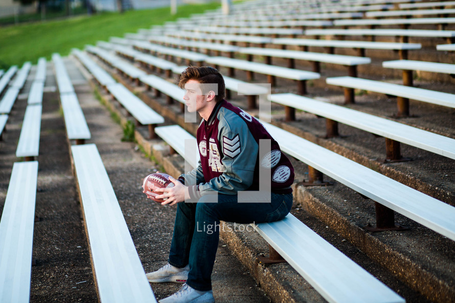 a young man sitting on bleachers holding a football 