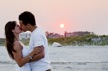 A man and woman kissing on a beach.