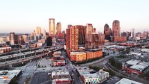 Aerial video of downtown Dallas, Texas during sunrise with highways, traffic and skyscraper buildings in the background.