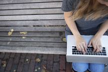 woman sitting on a bench with a laptop on her lap 
