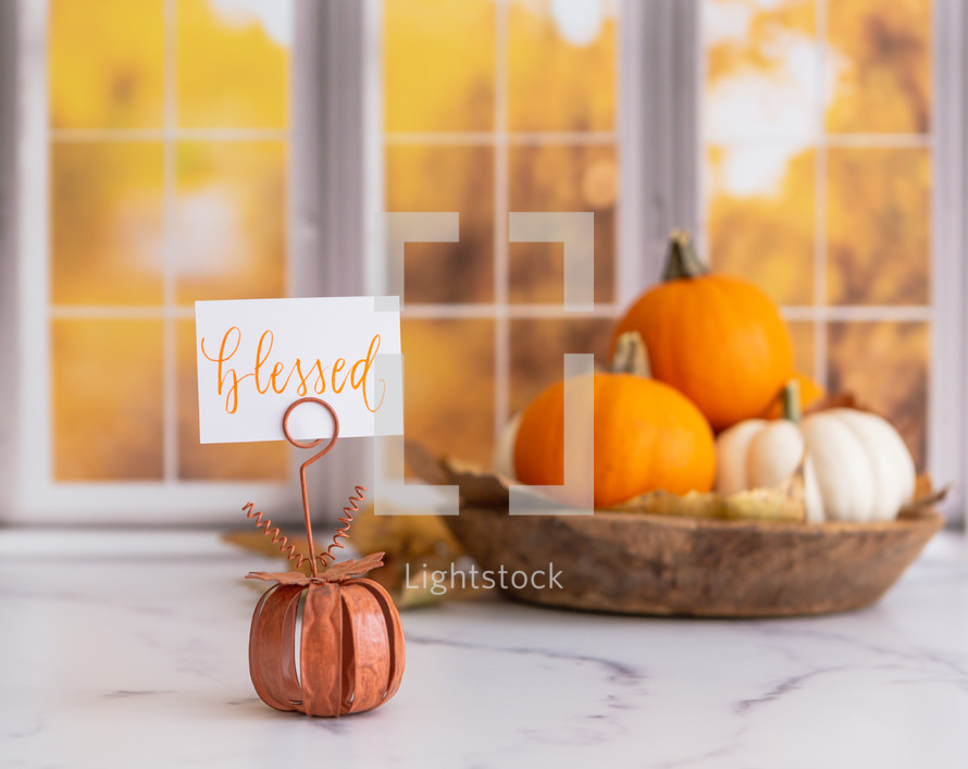 Orange and white pumpkins with a blessed sign in front of autumn window