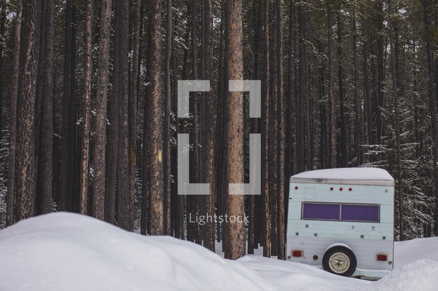 a tiny camper in the snow in a tall forest at a retreat centre
