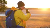 Hiker young tourist enjoying nature, drinking hot tea at sunset. Traveler young man drinking hot tea from stainless steel mug while on hike in forest. Active lifestyle traveling hiking adventure.
