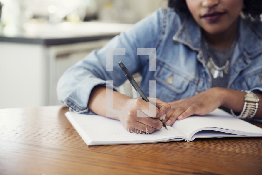 an African American woman sitting at a table writing in a journal 