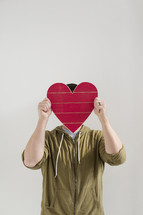 a man covering his face with a red wooden heart cut out 