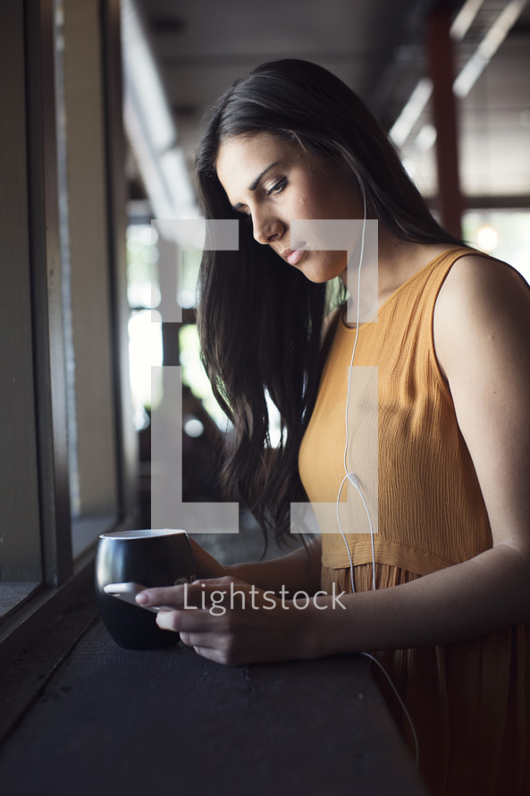 a young woman listening to earbuds in front of a window 