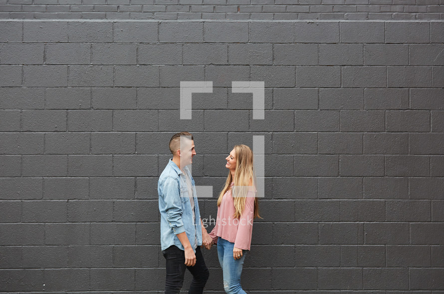 a couple standing in front of a gray wall holding hands 