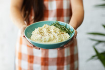 a woman holding a serving bowl of mashed potatoes 