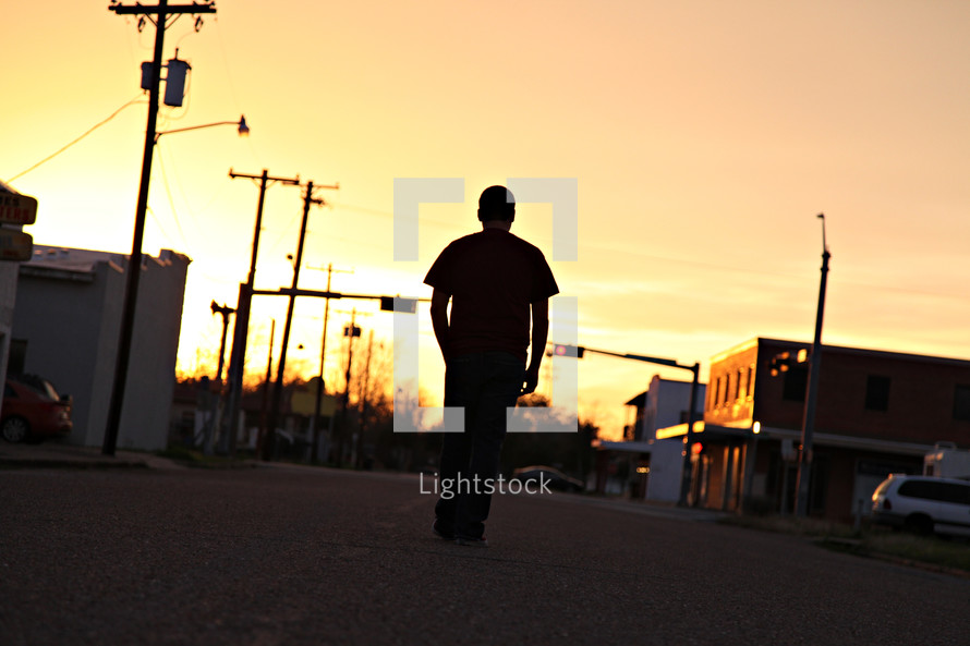 silhouette of a man standing in the middle of a street at sunset 