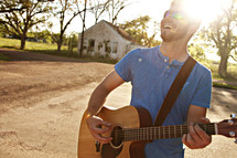 A young man on a country road playing a guitar.