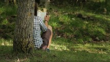 woman leaning against a tree reading a Bible 