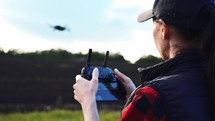 Woman farmer in hat standing in green wheat field and controlling of drone which flying above margin. Technologies in farming. Innovations for increasing productivity in agriculture.