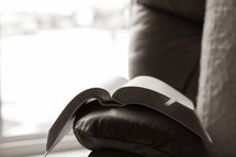 Bible open and resting on arm of leather chair by window
