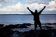 silhouette of a man with raised hands on a beach 