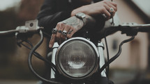 a man with tattoos on his hand sitting on a motorcycle 