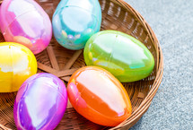 Plastic Easter eggs sitting in a circular brown basket on a textured background