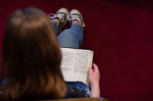 View over shoulder of a young woman or teen sitting on floor of a church meditating on scripture, I Thessalonians 5 - Christian conduct. Optional copy space on right.