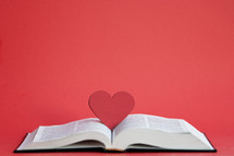 Close up red heart on an open Bible with a red background and copy space