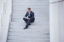 a businessman with a tablet sitting on steps 