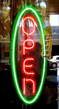 A Neon green and red Open sign in a window showing a retail business that is open to the public for customers. In this day and age, it is a welcome sign to see small businesses prosper and survive the time of COVID 19 to bring in customers and repeat business to the community.  