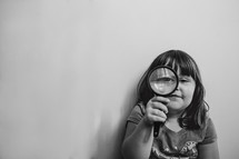 a girl child looking through a magnifying glass 