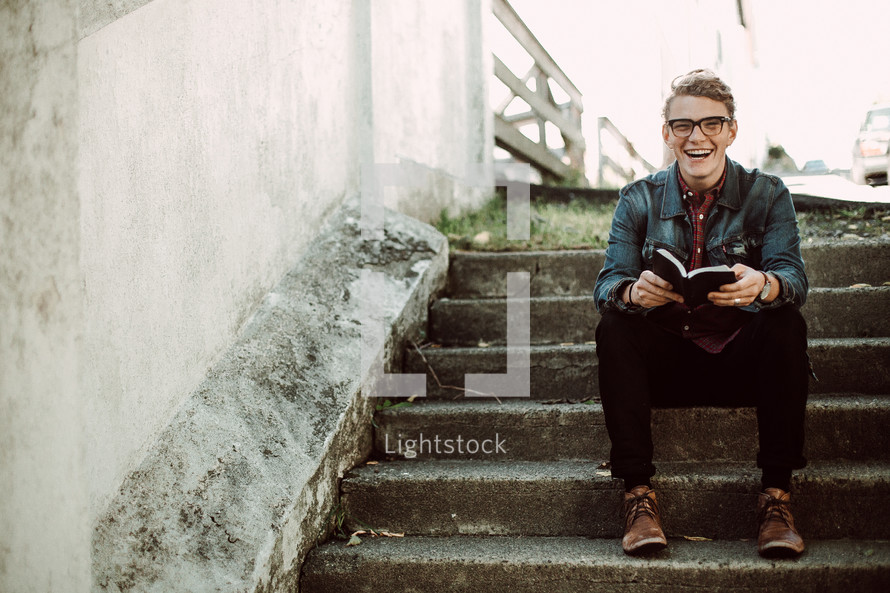 a young man sitting on steps holding a Bible 