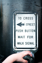 A little boys hand pressing the cross street button at a crosswalk.
