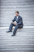 a businessman sitting on steps holding a tablet 