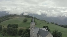 Aerial shot of beautiful gothic church with green hills and mountains in background 