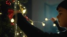 boy putting lights on a Christmas tree 