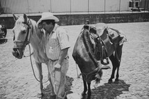 A exhausted man in a cowboy hat leans against his horse